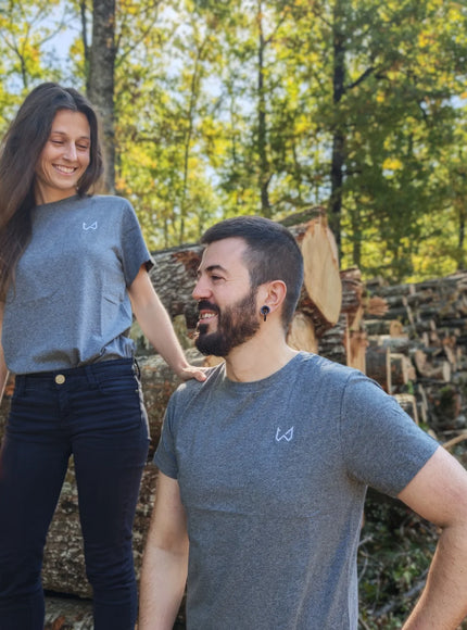 Two people standing in a forest with stacked logs around them wearing hemp and organic cotton tshirt.