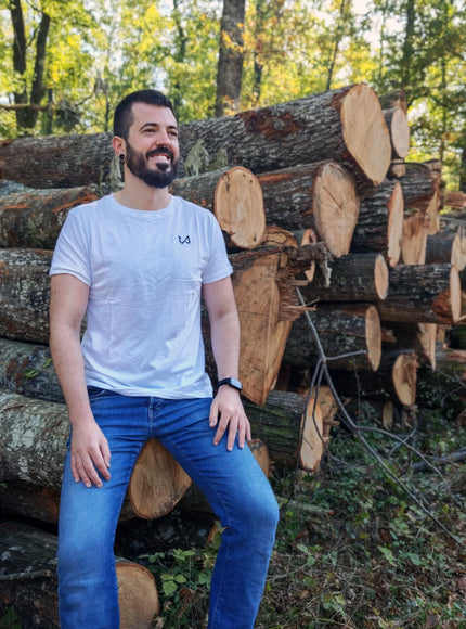 Man sitting among stacked logs in a forest wearing hemp and organic cotton tshirt.