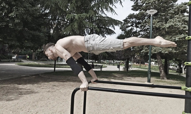 Person performing a full planche on a park bar with trees and benches in the background