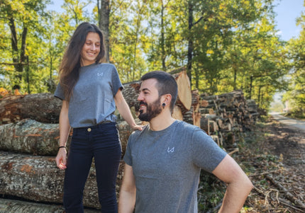 Two people standing in a forest with stacked logs around them wearing hemp and organic cotton tshirt.