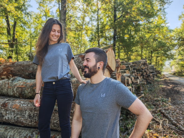 Two people standing in a forest with stacked logs around them wearing hemp and organic cotton tshirt.