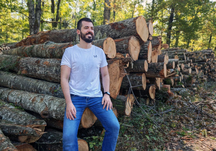 Man sitting among stacked logs in a forest wearing hemp and organic cotton tshirt.