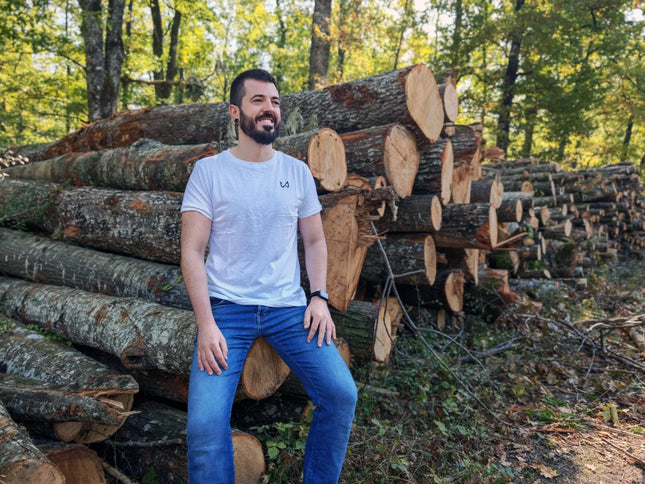 Man sitting among stacked logs in a forest wearing hemp and organic cotton tshirt.