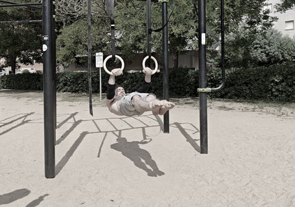 Calisthenics athlete doing a front lever on wooden rings wearing protective elbow sleeves in an urban workout park with a blurred background