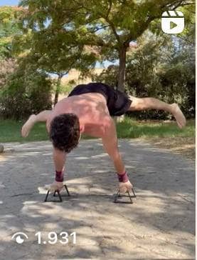 Atleta maschio che esegue la planche a gambe divaricate sulle parallele