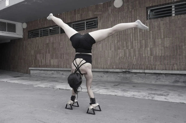 Athlete performing a handstand on parallettes in an urban setting