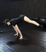 Person in black athletic wear performing a handstand on a dark floor.