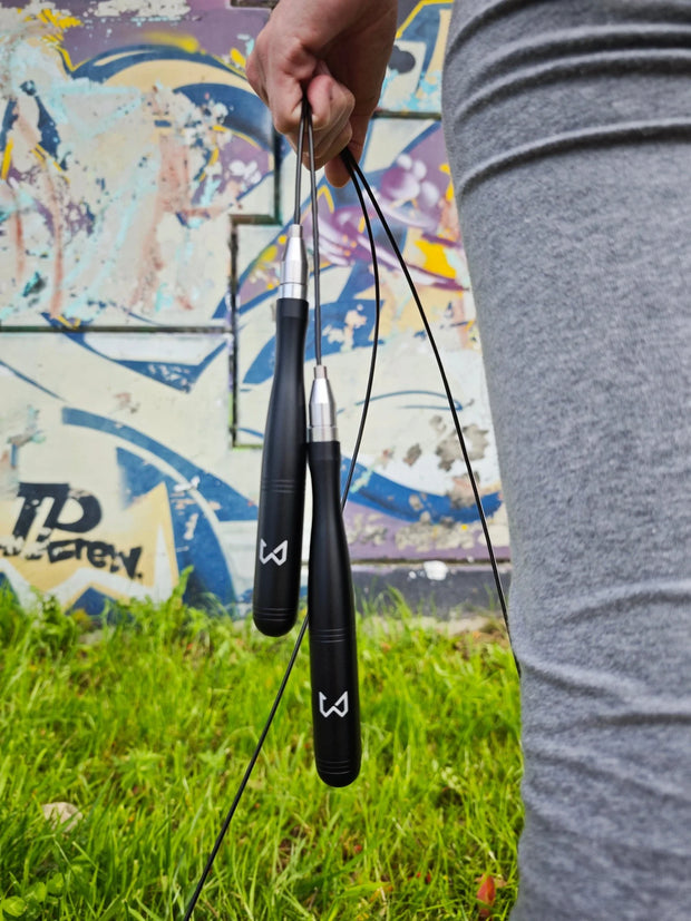 Person holding two black jump ropes with a colorful mural in the background