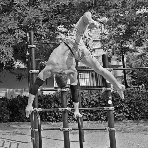 Person doing a handstand on outdoor gym equipment with trees and building in the background