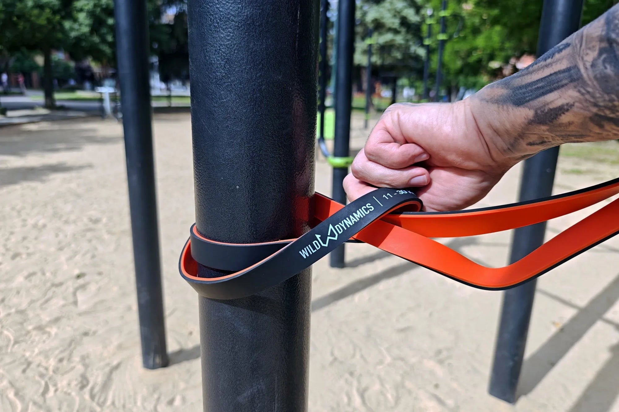 Person using wild dynamics resistance band on outdoor exercise equipment