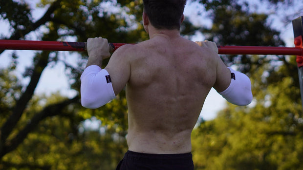 Person doing pull-ups outdoors wearing elbow sleeves