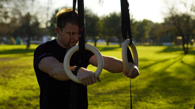 Person using gymnastic rings outdoors in a park setting