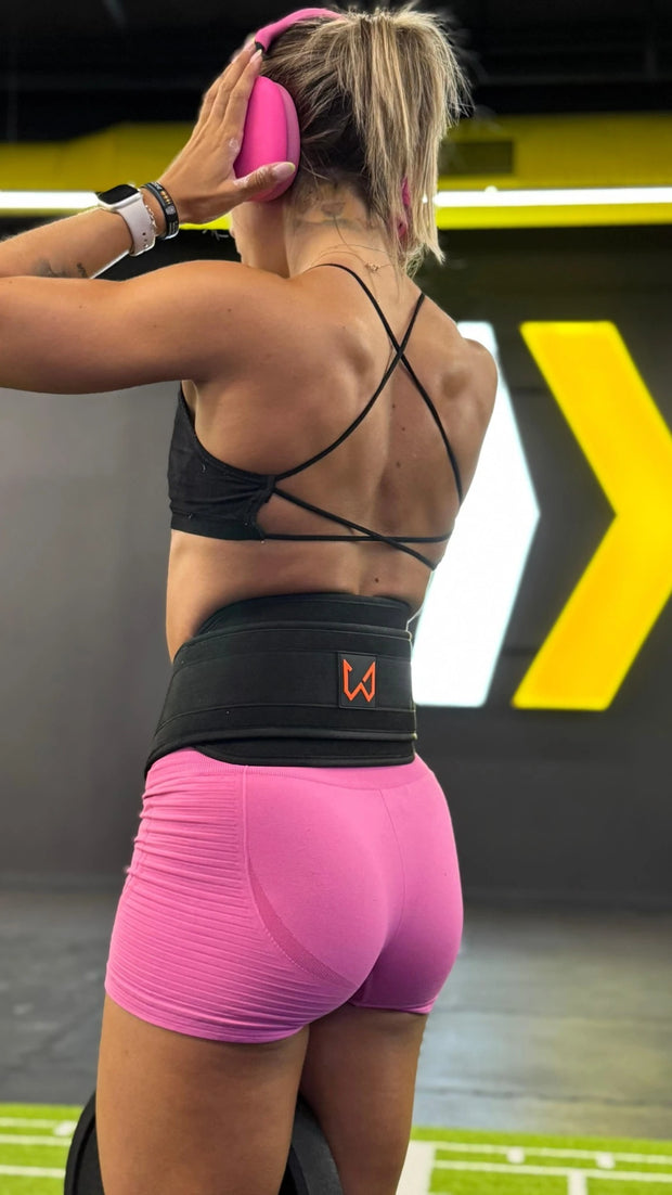Person wearing a black sports bra and pink shorts exercising with a dip belt of wild dynamics