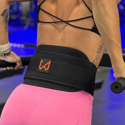 Person exercising with a black dip belt featuring an orange logo in a gym setting.