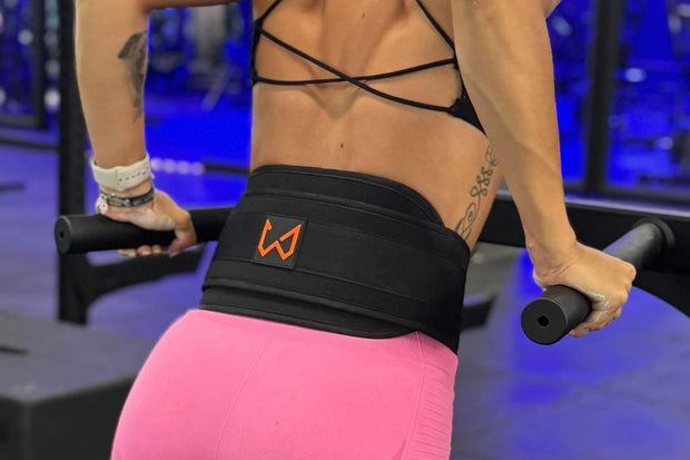 Person exercising with a black dip belt featuring an orange logo in a gym setting.