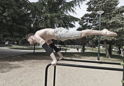 Person performing a full planche on a park bar with trees and benches in the background