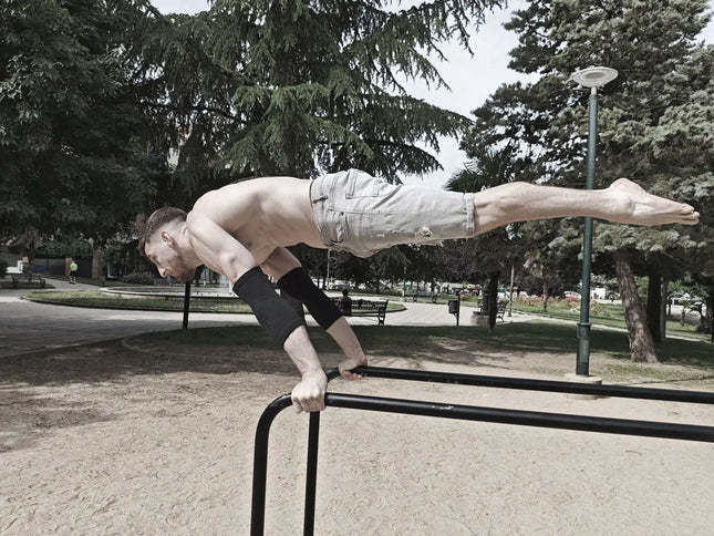 Person performing a full planche on a park bar with trees and benches in the background