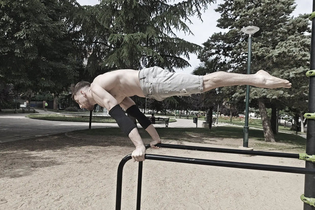 Person performing a full planche on a park bar with trees and benches in the background