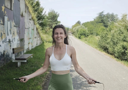 Woman exercising with a jump rope on a path next to a graffiti-covered wall.