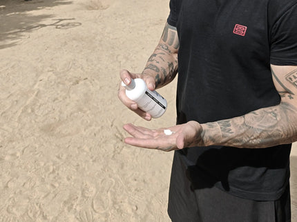 Person applying liquid chalk to hands outdoors on a sandy surface