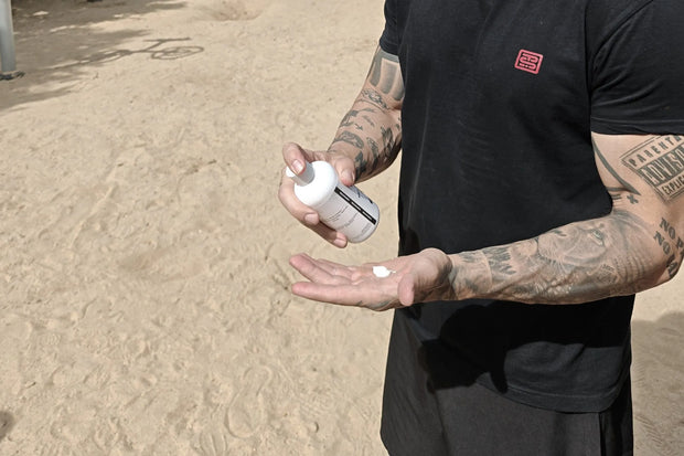 Person applying liquid chalk to hands outdoors on a sandy surface